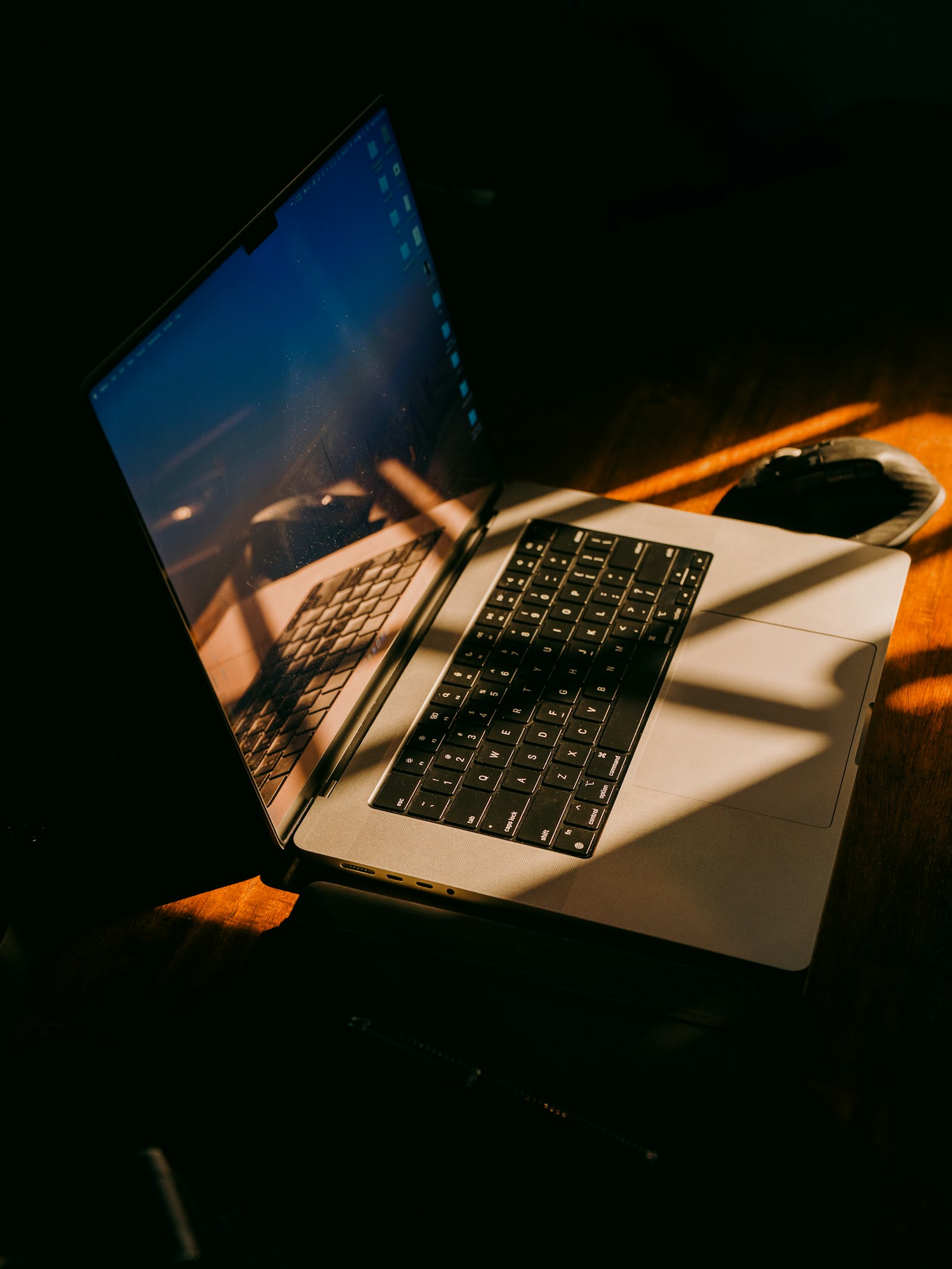 A laptop on a warm wooden desk, lit by golden afternoon light through the blinds.